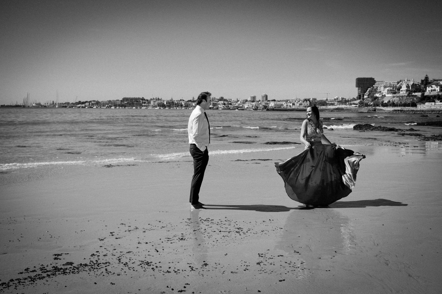 A series of black and white beach photographs showing people walking and relaxing along the shoreline on a sunny day.