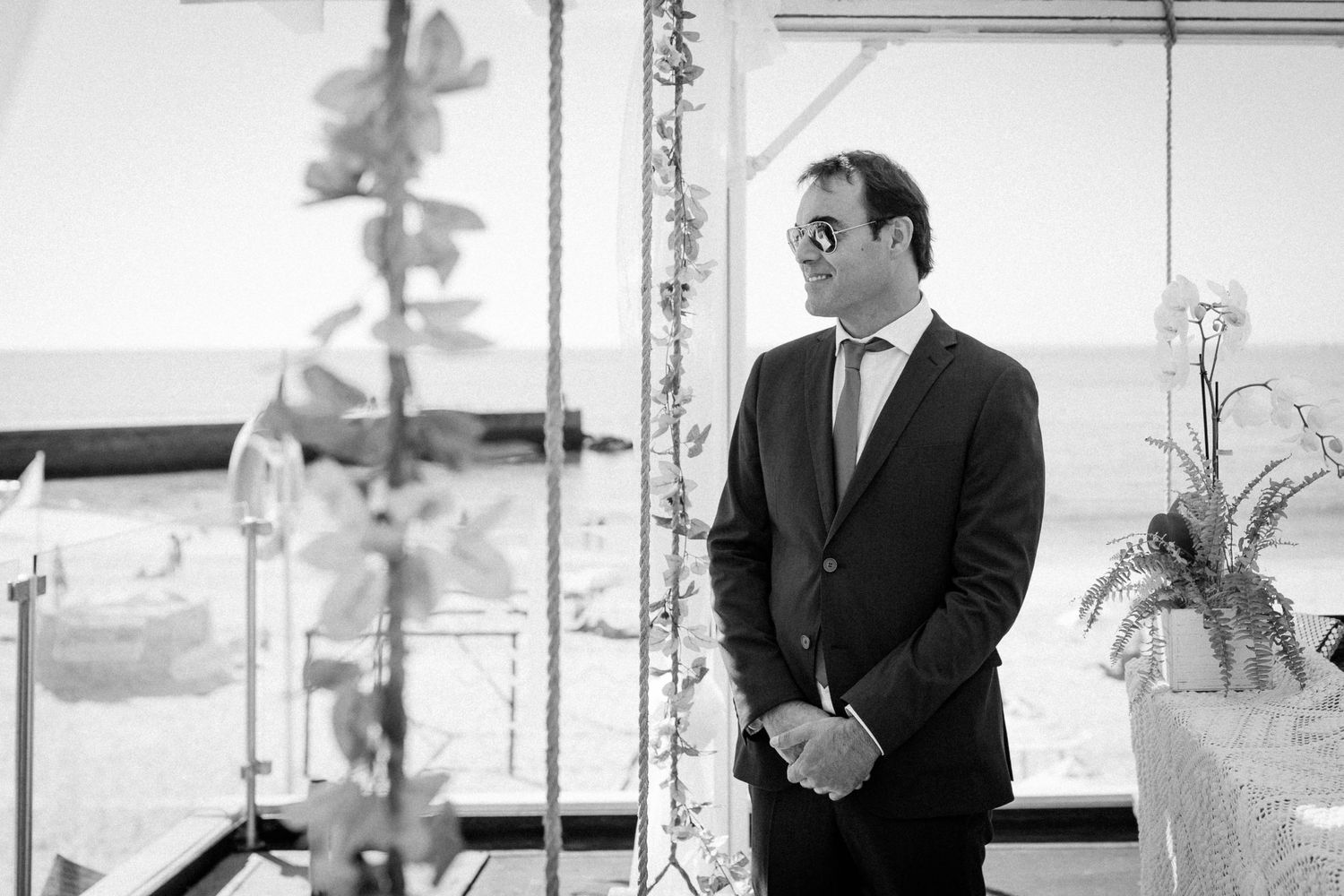 A black and white photograph shows a person in a suit standing next to a potted plant in an office setting.