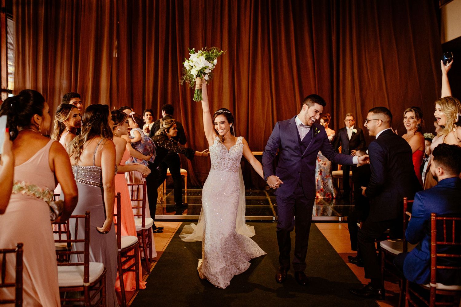Newlyweds making their grand exit down the aisle with guests cheering.