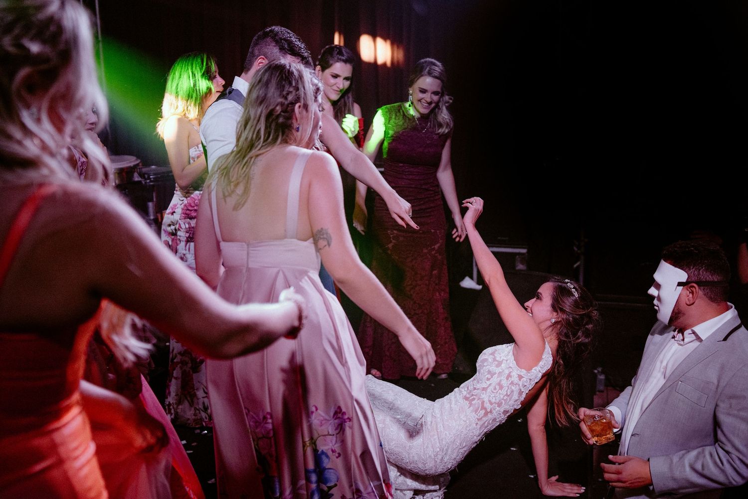 People dancing and celebrating at a wedding reception with colorful lighting and festive atmosphere.