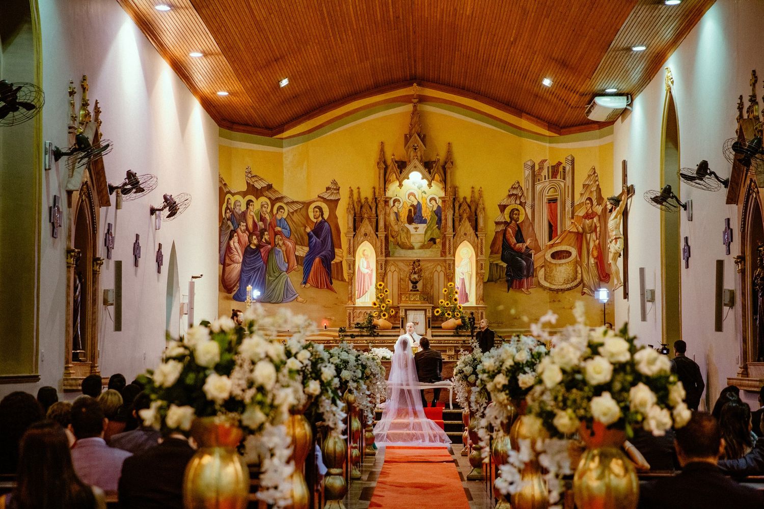 Ornate church interior decorated with white flowers and religious artwork for a wedding ceremony.