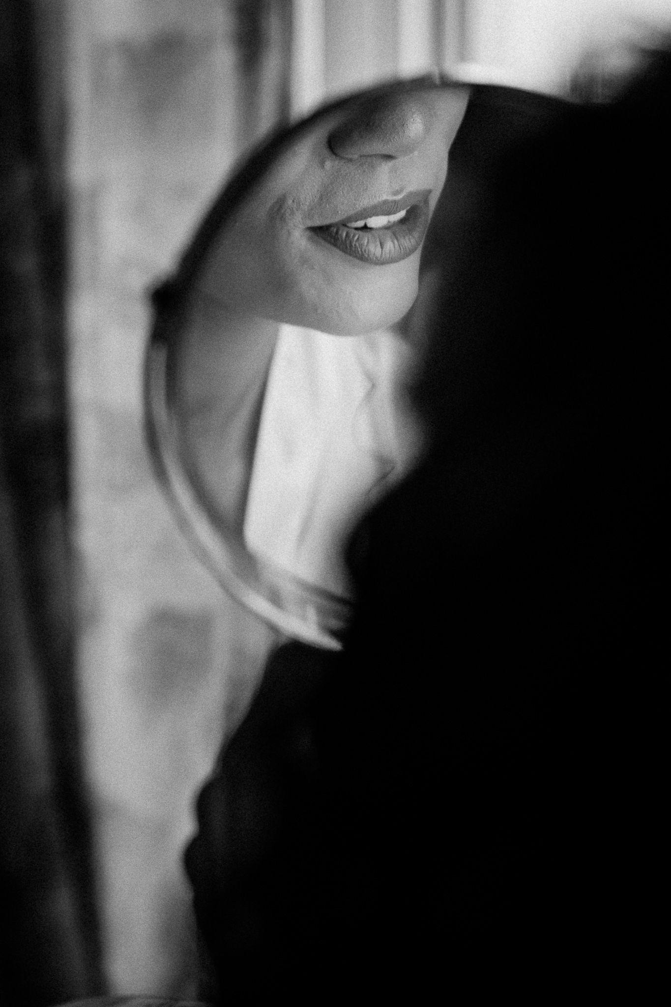 Black and white photo of a woman's smile reflected in a round mirror, with soft light and artistic shadows.