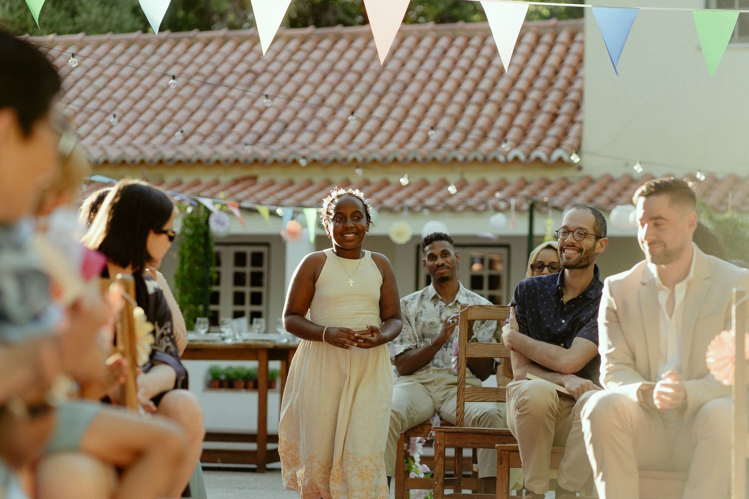Diverse group of guests enjoying an outdoor wedding reception with colorful bunting flags and rustic venue backdrop.