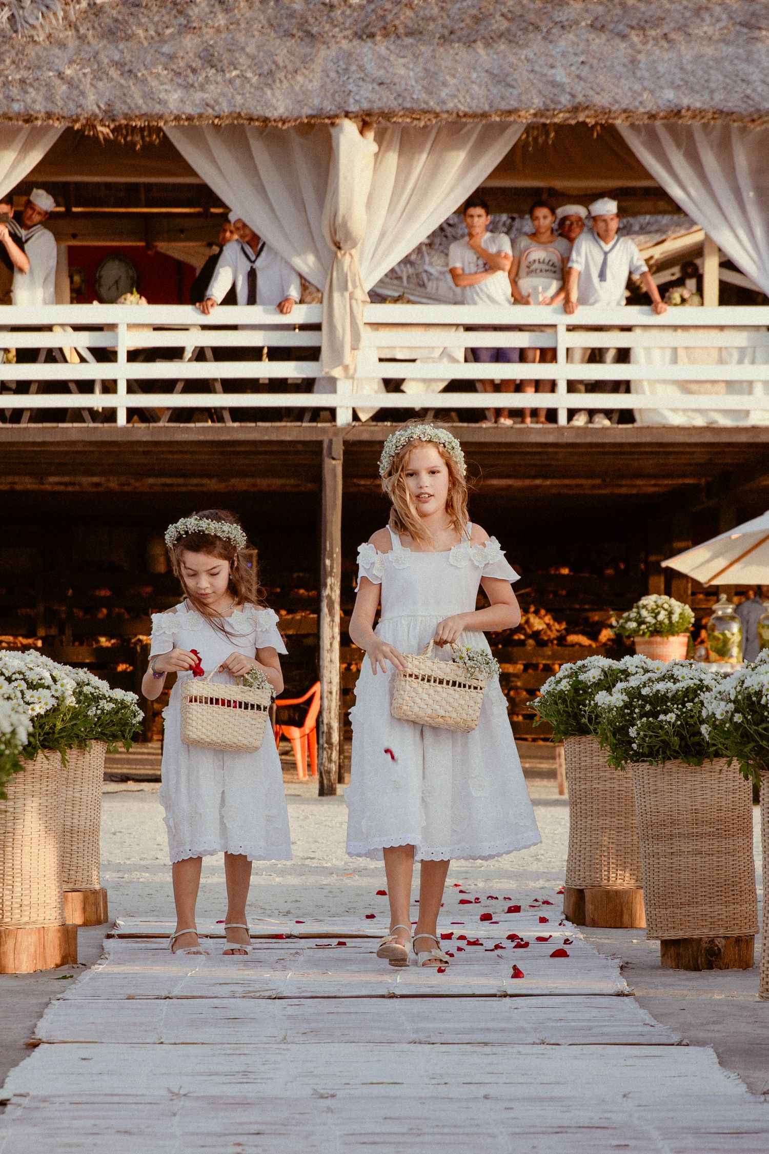 Series of flower girls at a rustic barn wedding venue walking and spreading rose petals along a painted white aisle.
