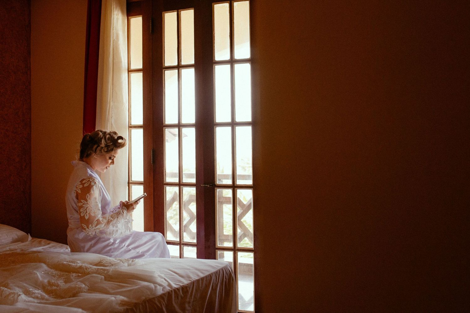 A person stands by large French doors letting sunlight stream through the elegant white curtains in a peaceful room.
