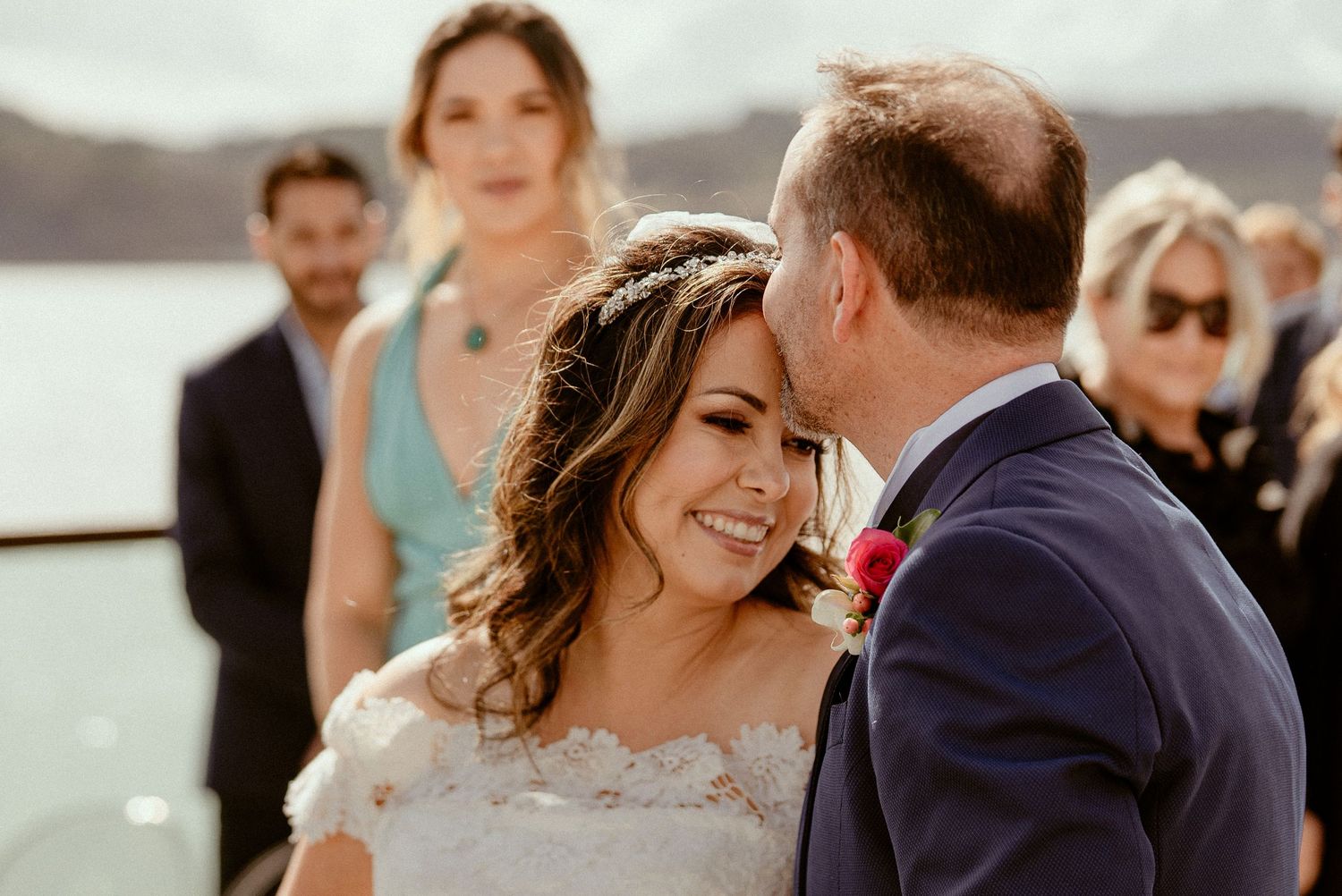Newlyweds share an intimate moment during their lakeside wedding ceremony as guests look on in the background.
