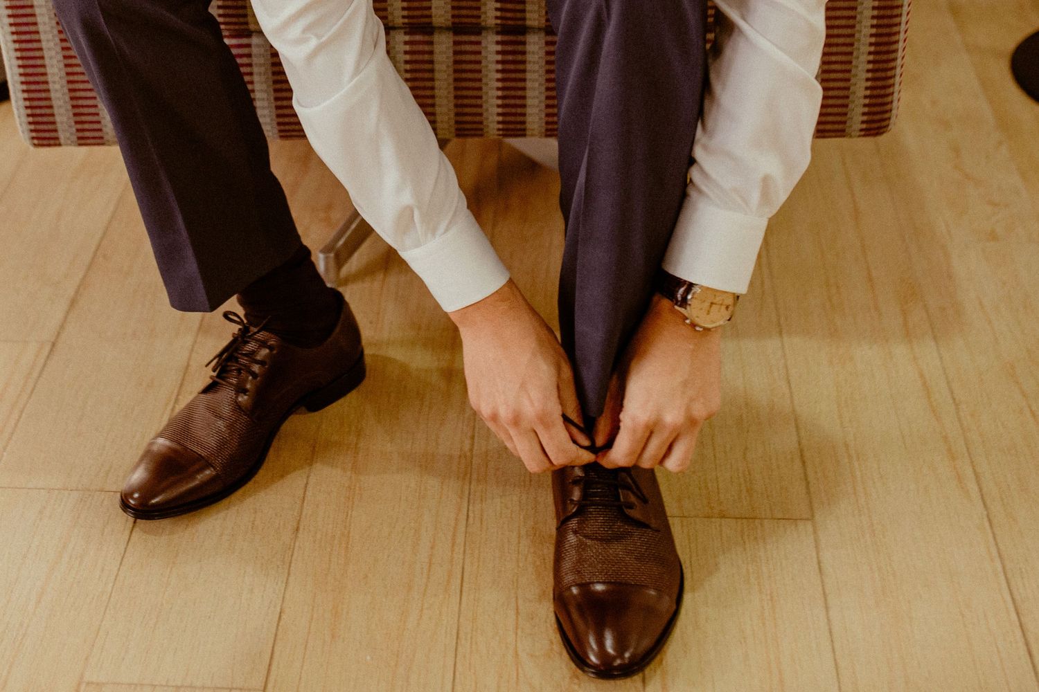 Close-up view of dress shoes and pant legs of people sitting in a row at a formal gathering or event.