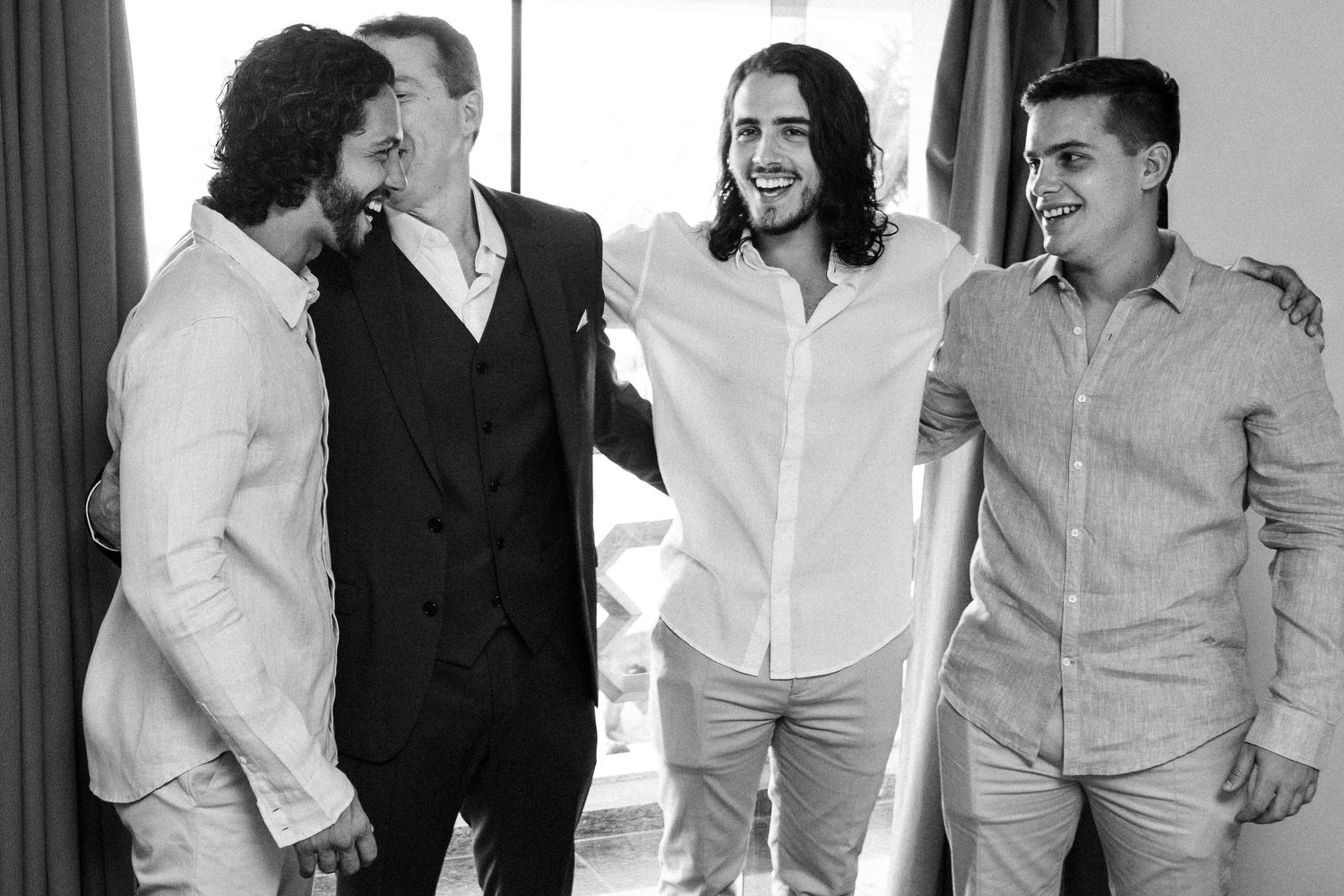 A group laughs together wearing formal attire in black and white photography.