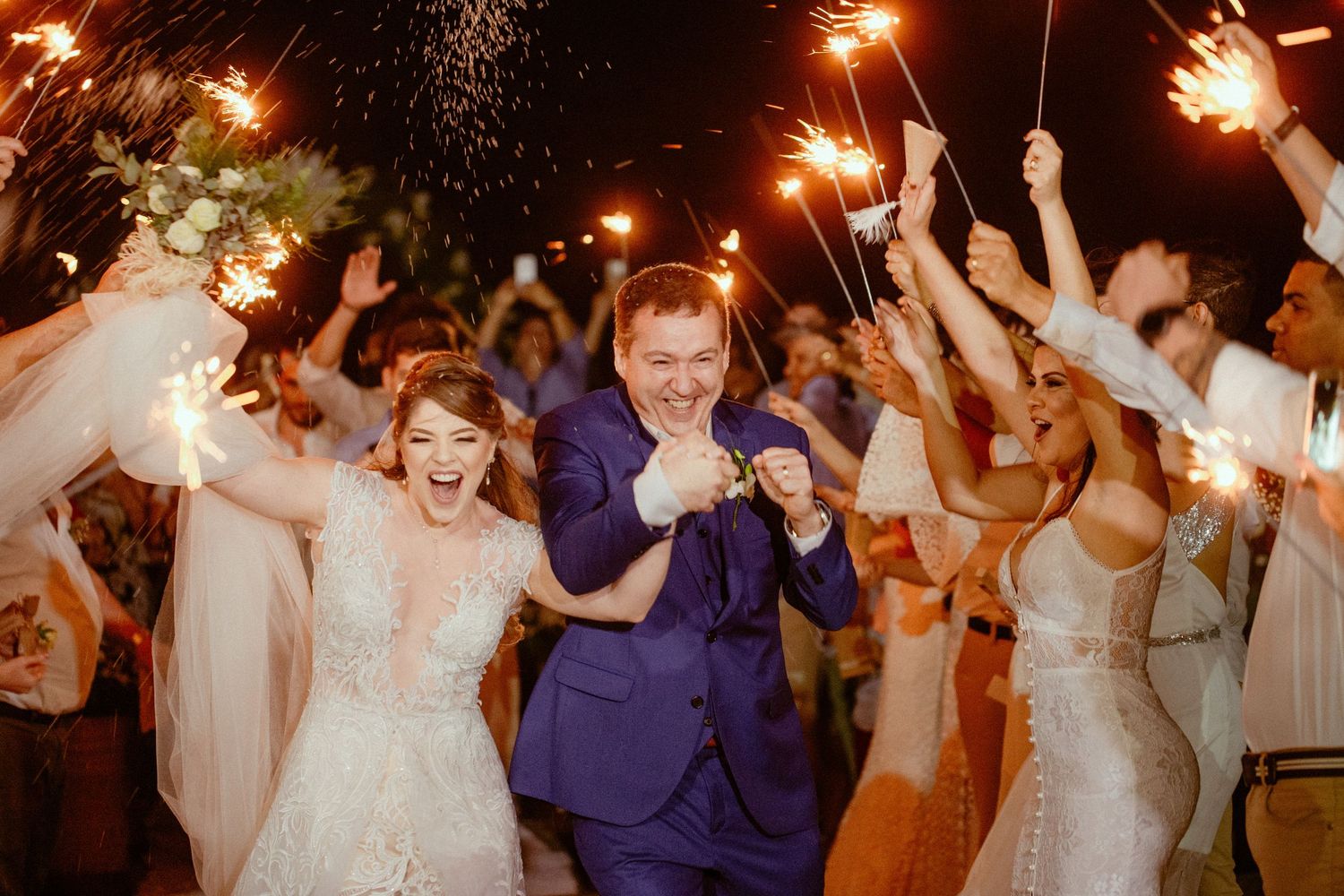 Wedding guests dance and celebrate with sparklers in hand during an evening reception celebration.