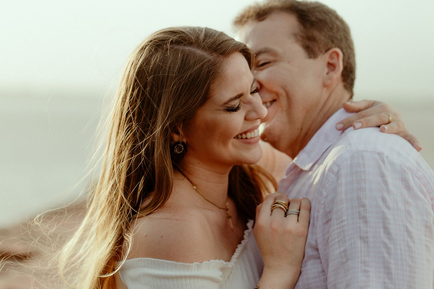 A romantic couple embraces on a beach at sunset during their engagement photo session.