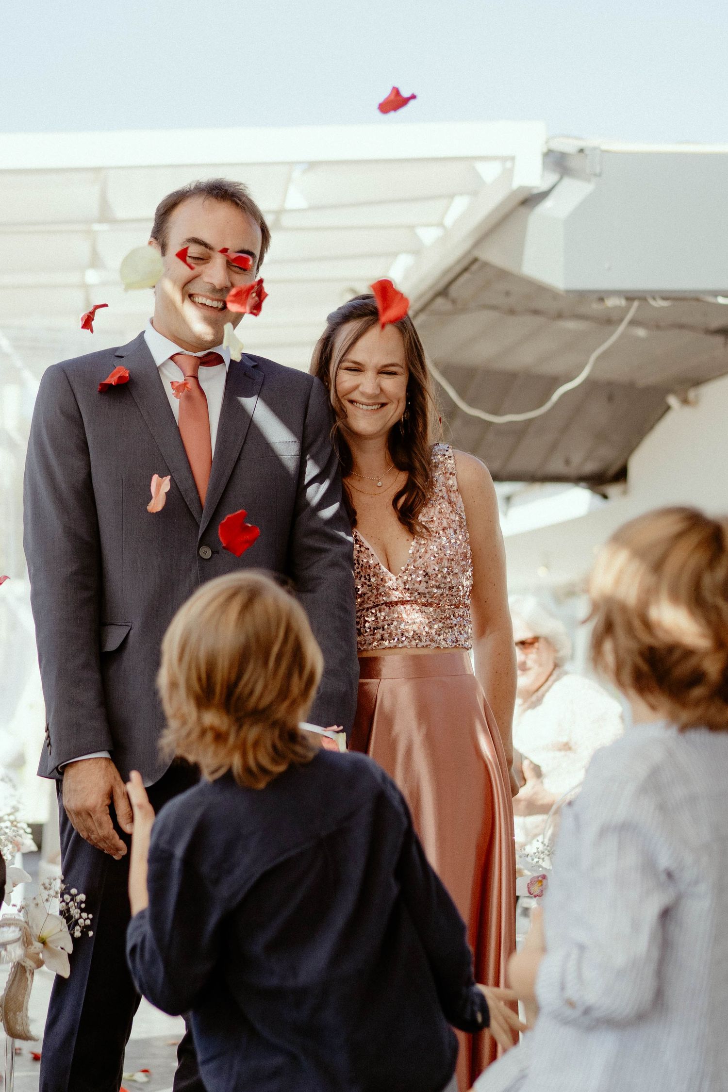 A celebration moment with red confetti falling as a couple stands together in formal attire at an outdoor event.