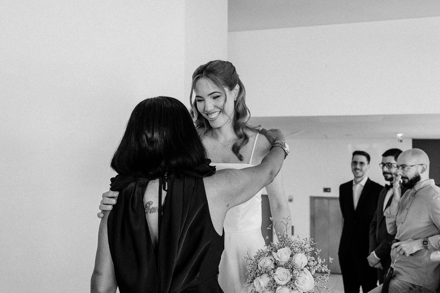 Black and white photo of a smiling bride holding bouquet embracing a guest at her wedding reception.