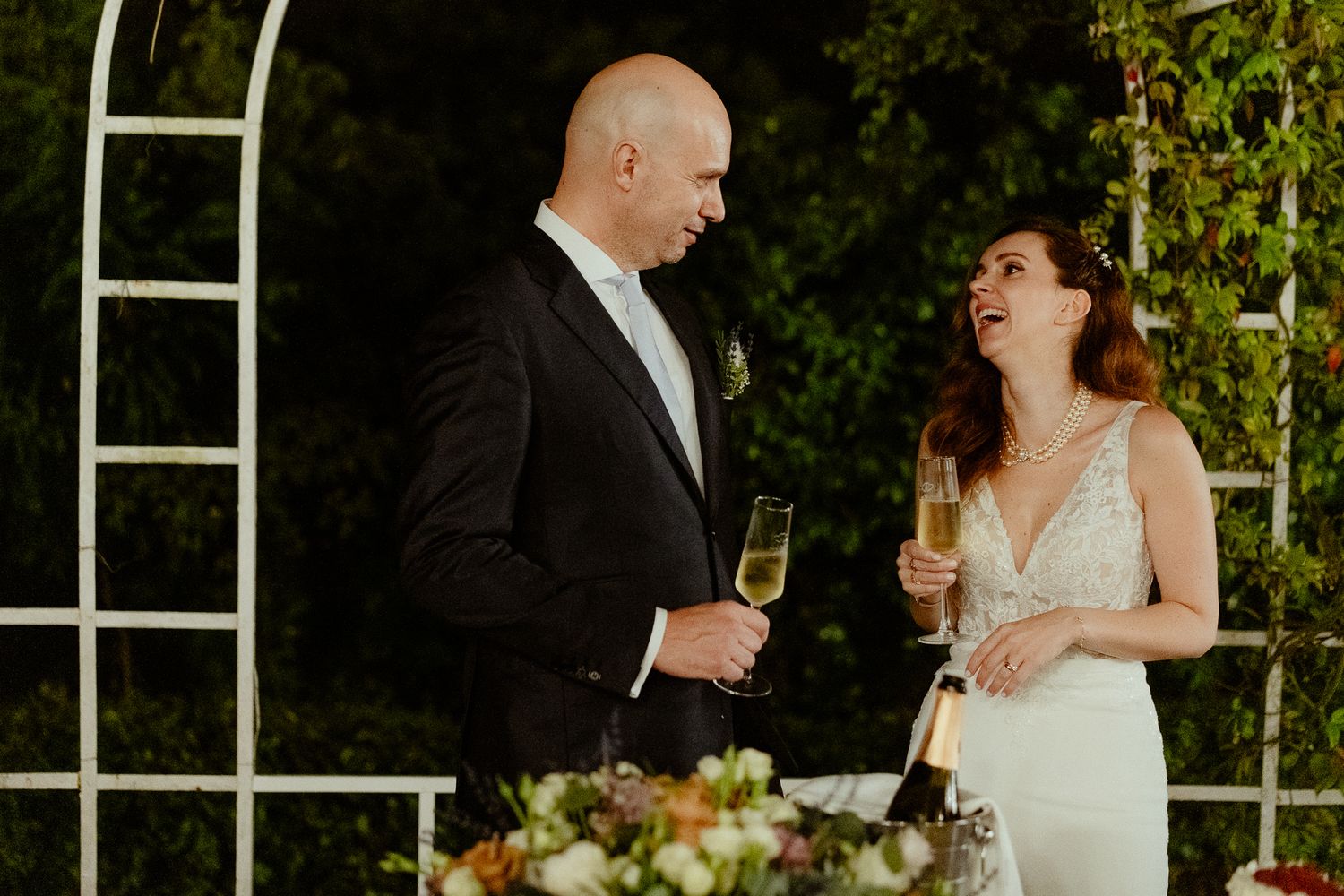 Bride and groom laughing and toasting with champagne glasses at their outdoor wedding reception.