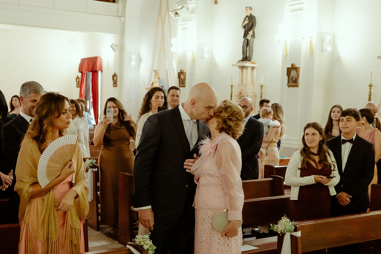 Elderly couple sharing a tender moment at a church wedding ceremony with guests seated in pews.