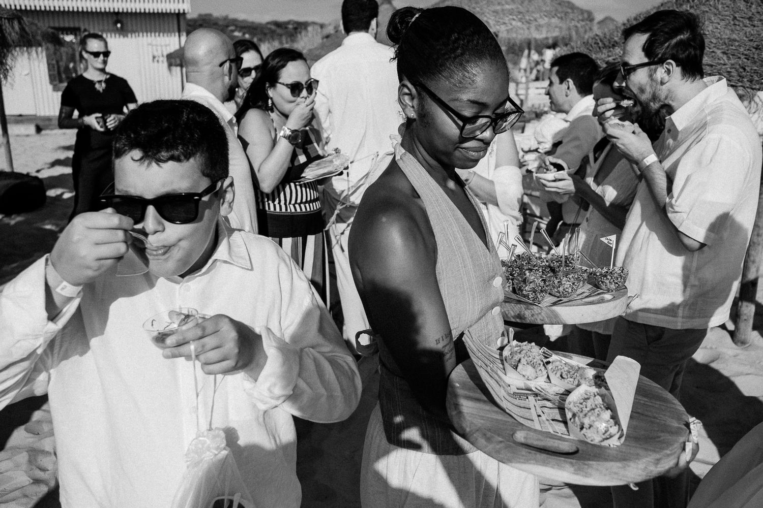 Black and white photo of guests enjoying food and drinks at an outdoor social gathering or wedding reception.
