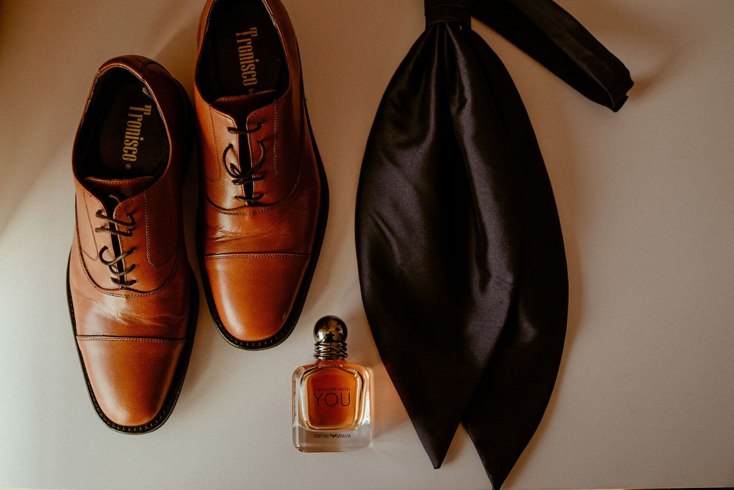 Stylish brown leather Oxford dress shoes and a black necktie arranged against a white background.