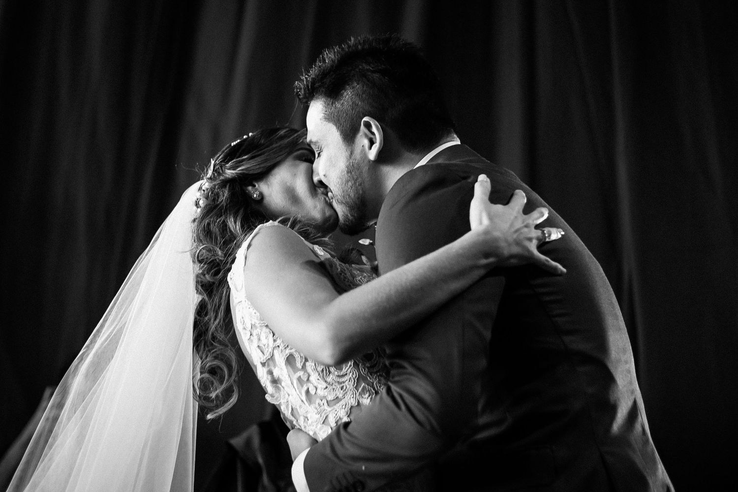 A romantic black and white wedding photo captures a couple embracing in a tender kiss during their special day.