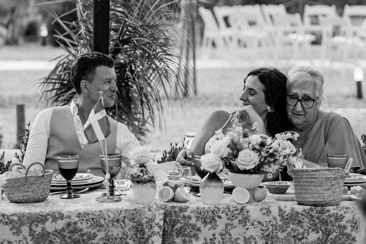 Black and white photo of wedding guests laughing together at an outdoor reception table.