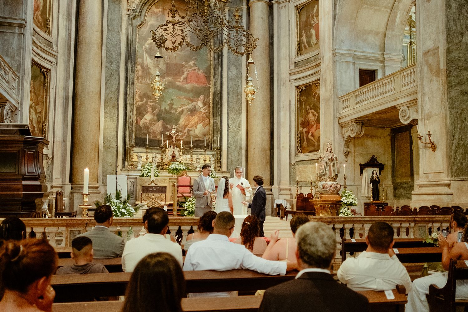 Elegant church wedding ceremony with guests seated in pews before ornate altar with floral arrangements.