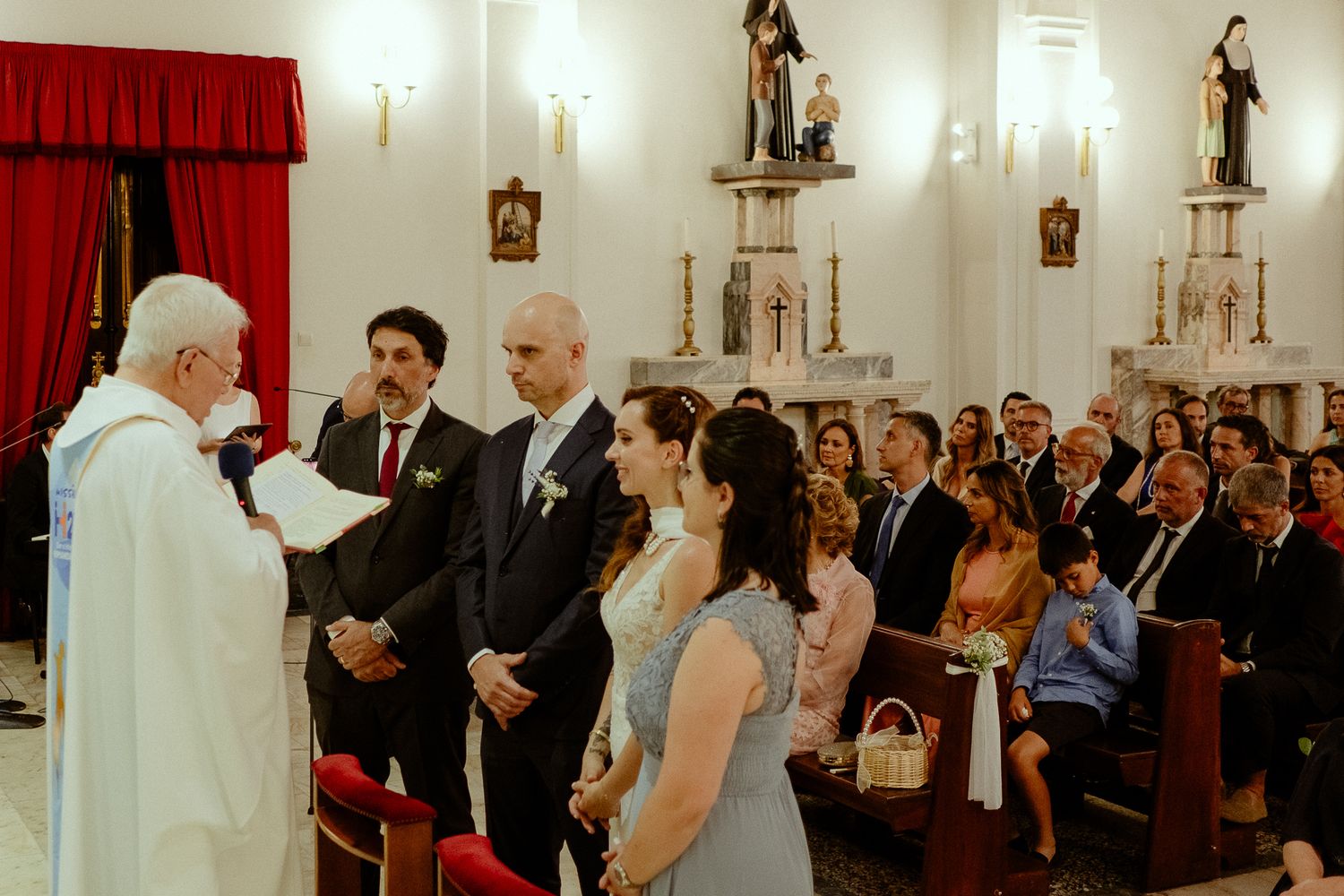 Wedding ceremony in a church with priest, couple, and guests gathered at the altar.