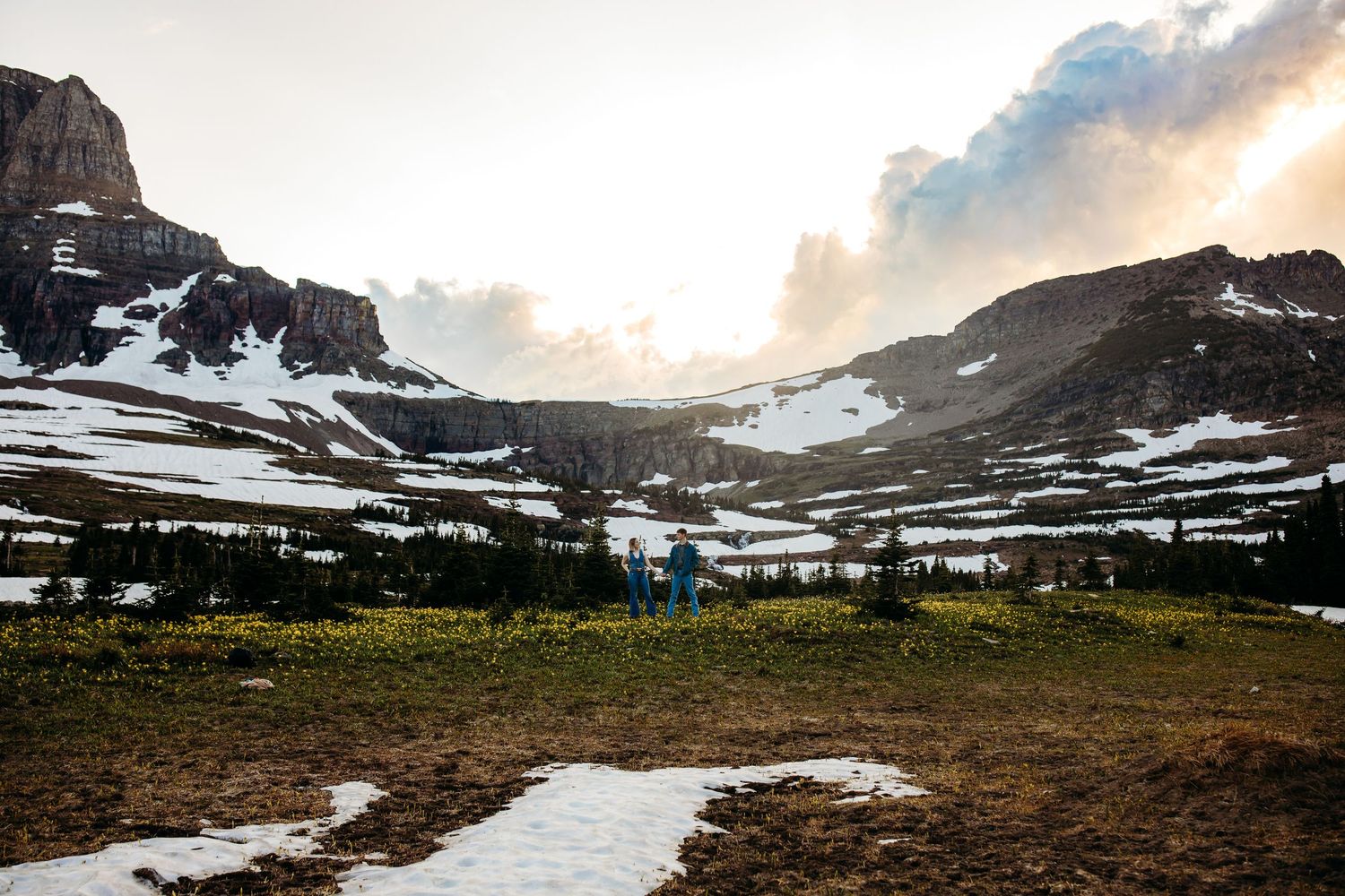A wide view of the mountains at Logan Pass, Glacier National Park, Montana. There is a couple in denim outfits between the mountains.