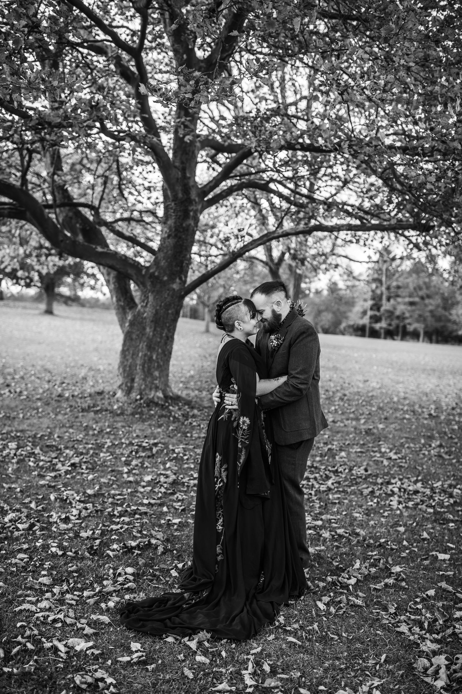 A wedding couple embraces face to face. The bride is wearing a black floral dress, and the groom has a brown suit on.