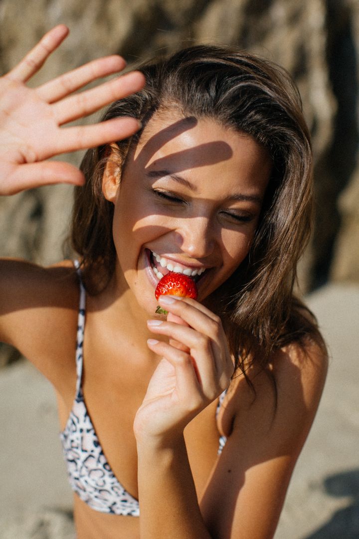 Creative model portfolio photo at Malibu beach of Black woman with hand blocking sun eating strawberry by LA photographer Phia Photography.