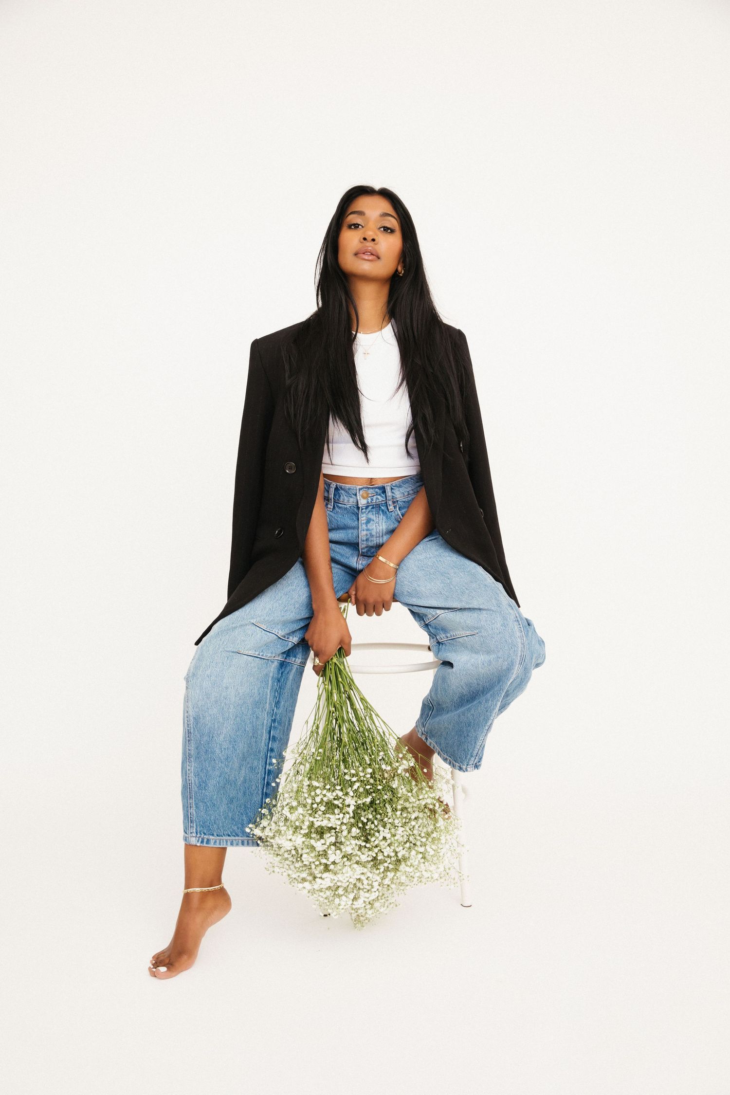 Woman with deep dark brown skin posed on stool with flowers for creative portraits in Santa Monica studio by photographer Phia Photography.