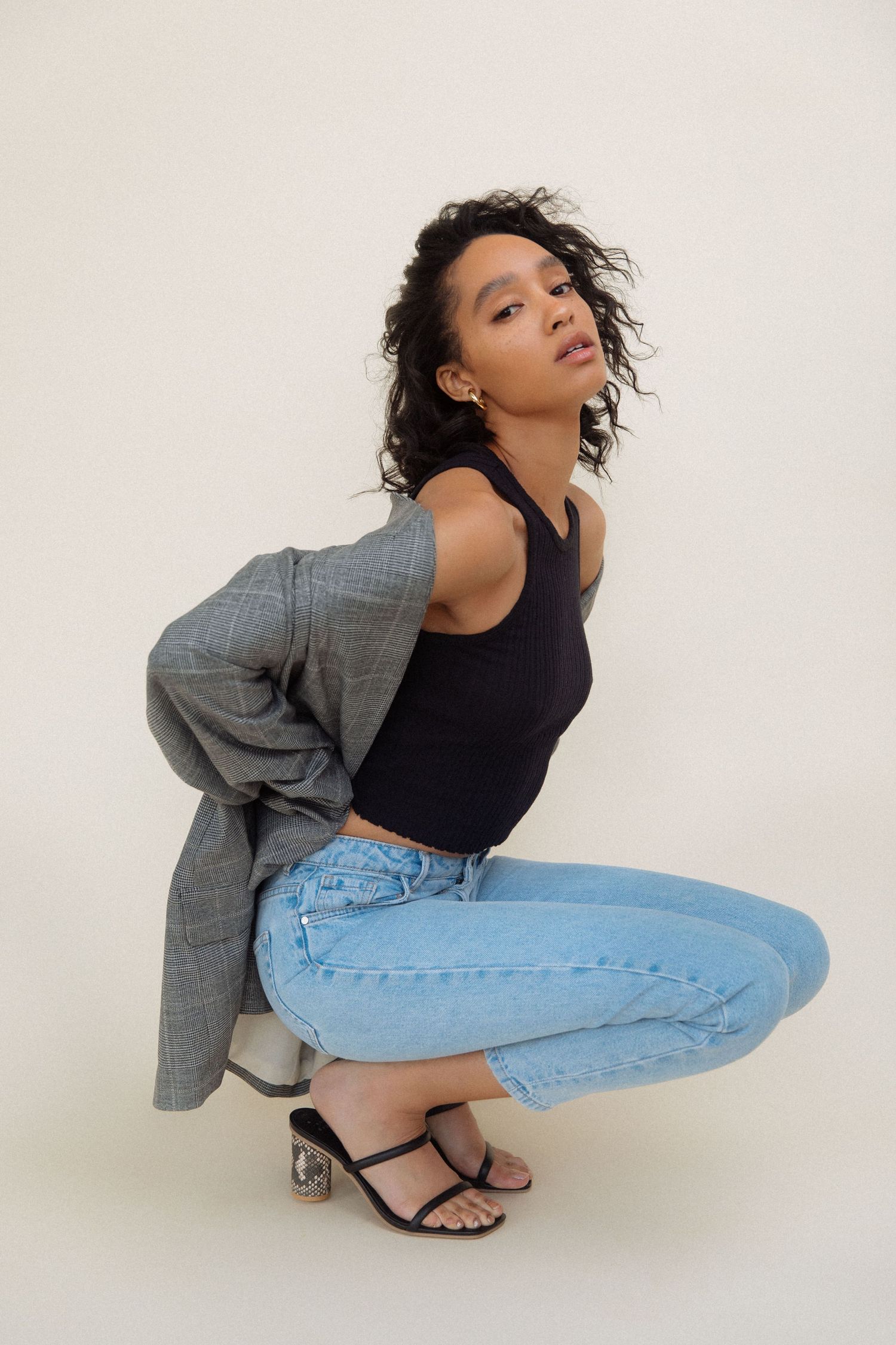 Editorial portrait of Black woman in denim jacket and jeans crouching in Los Angeles studio by Phia Photography.