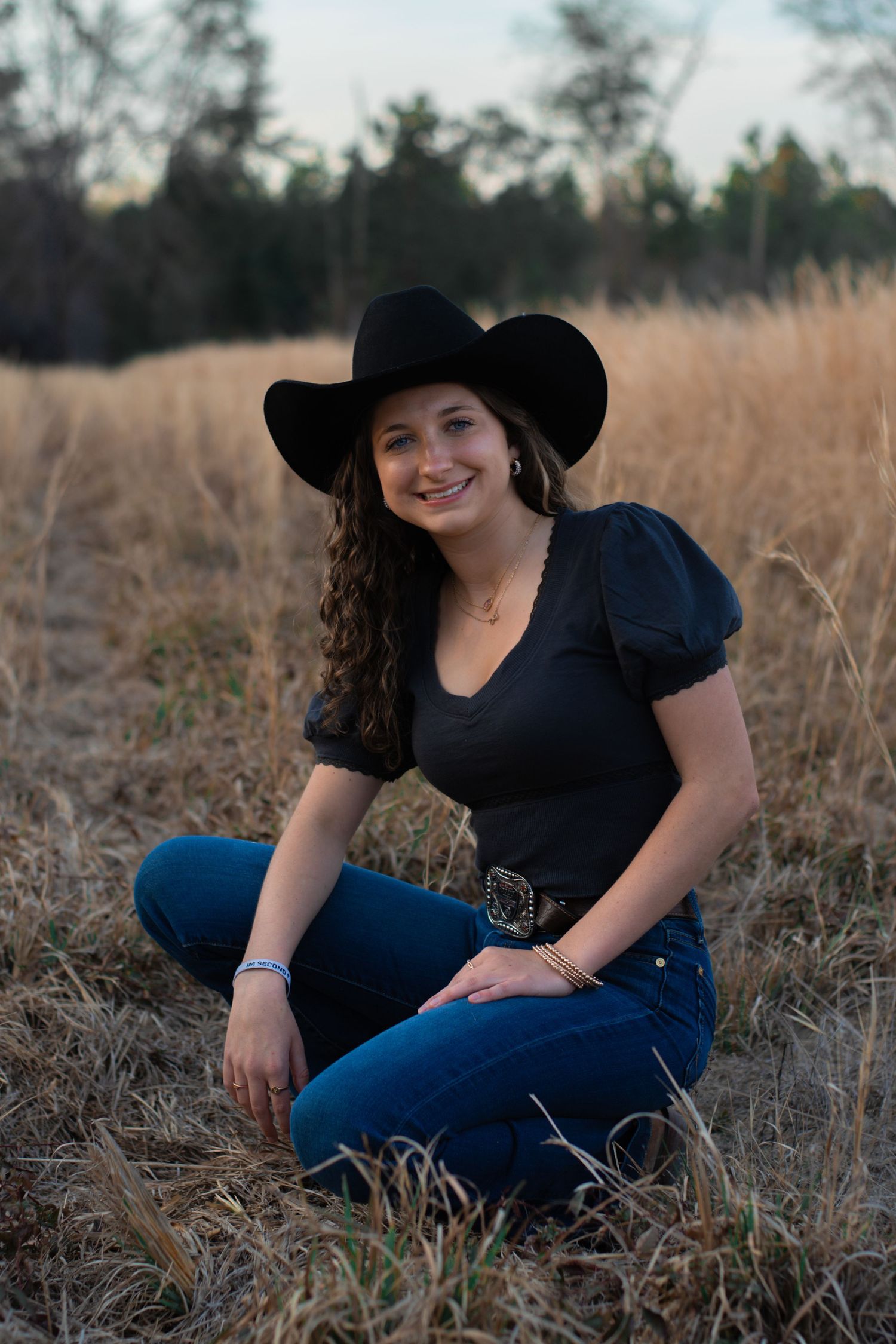 High school senior girl wearing black Stetson. Kneeling in grassy field in Early Branch, South Carolina.