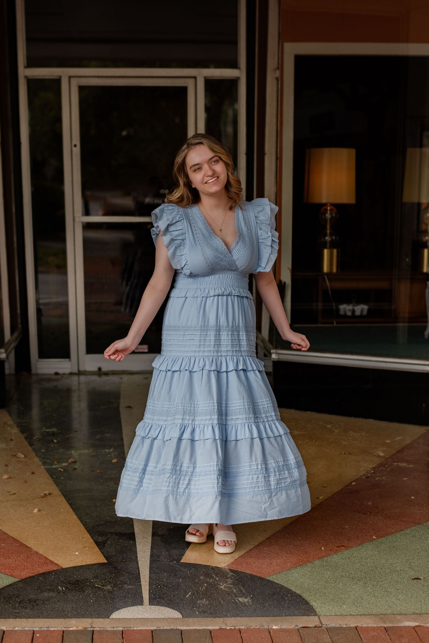 High school senior gal spinning in blue dress and wedges in front of storefront in downtown Walterboro, South Carolina