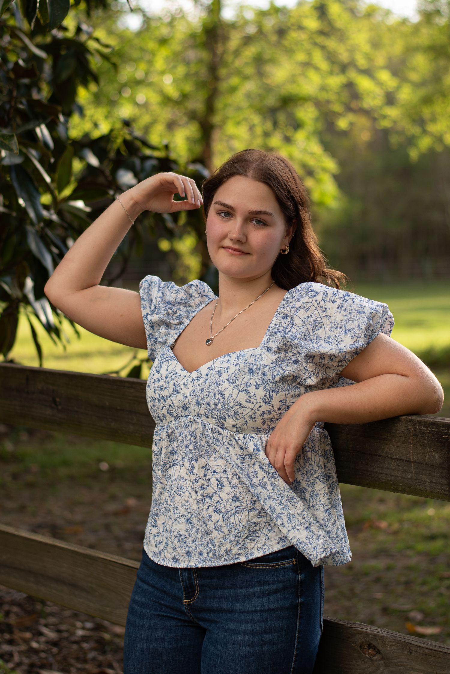 High school senior girl in front of horse pasture and fence on farm in Ridgeland, South Carolina.