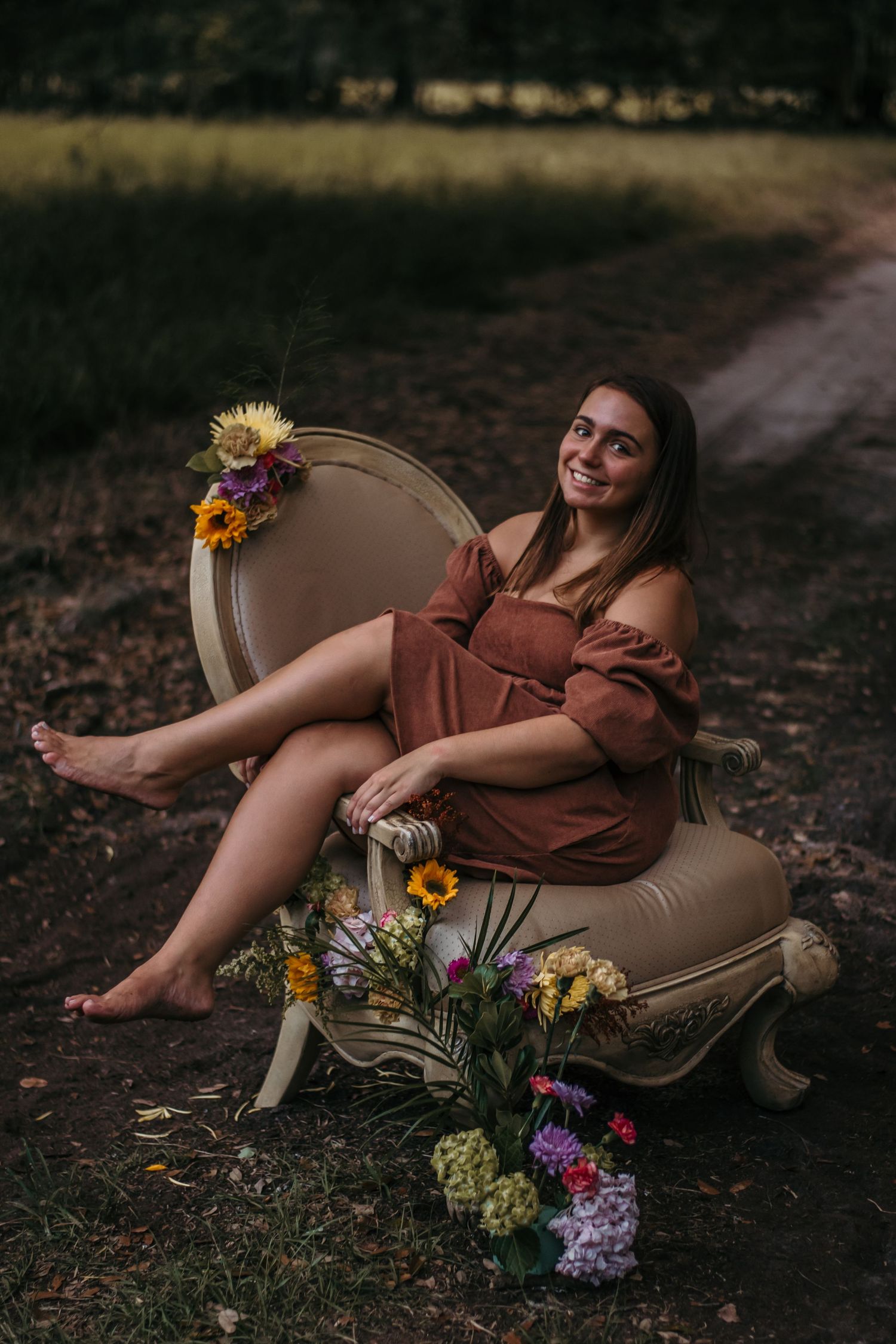 Barefoot high school senior girl sitting on flower covered chair in grassy pasture in Jasper County, South Carolina.