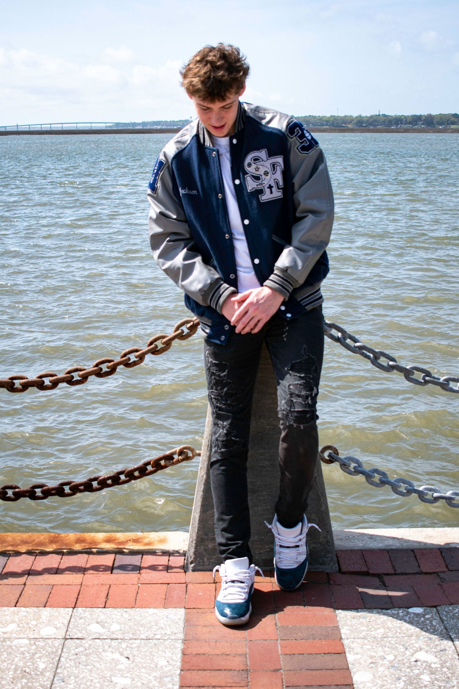 High school senior guy in letterman coat in front of water in the waterfront in downtown Beaufort, South Carolina.
