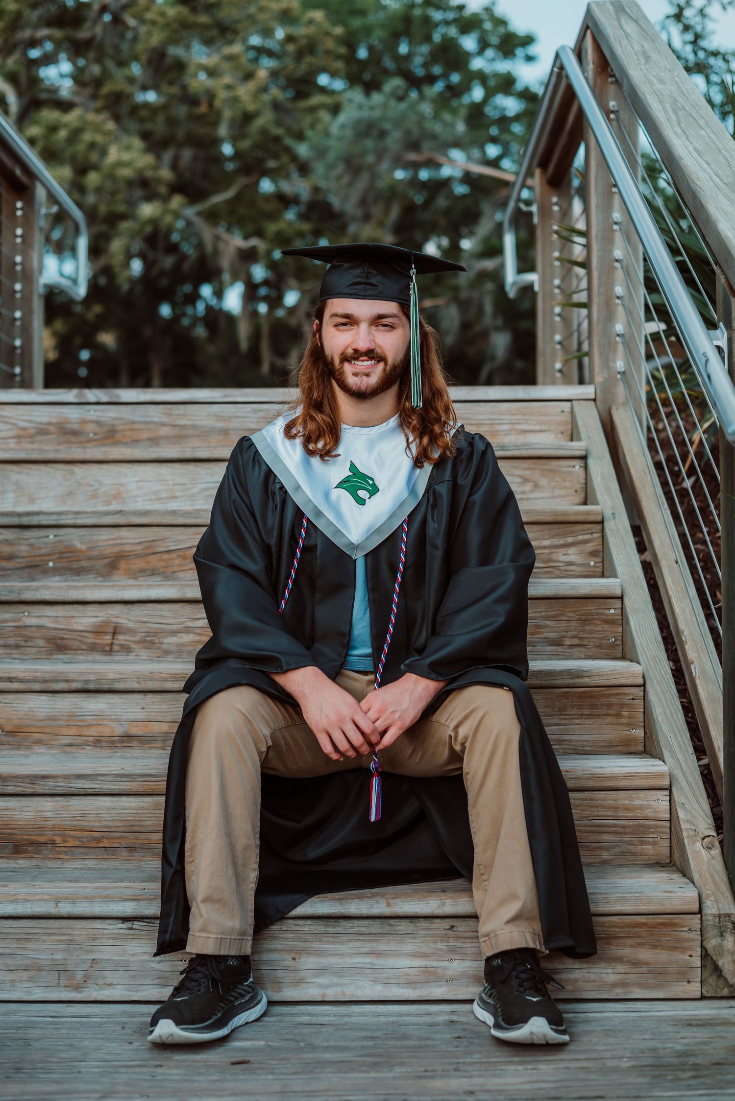 High school senior in Bluffton High School cap and gown sitting on steps in Old Town Bluffton, South Carolina