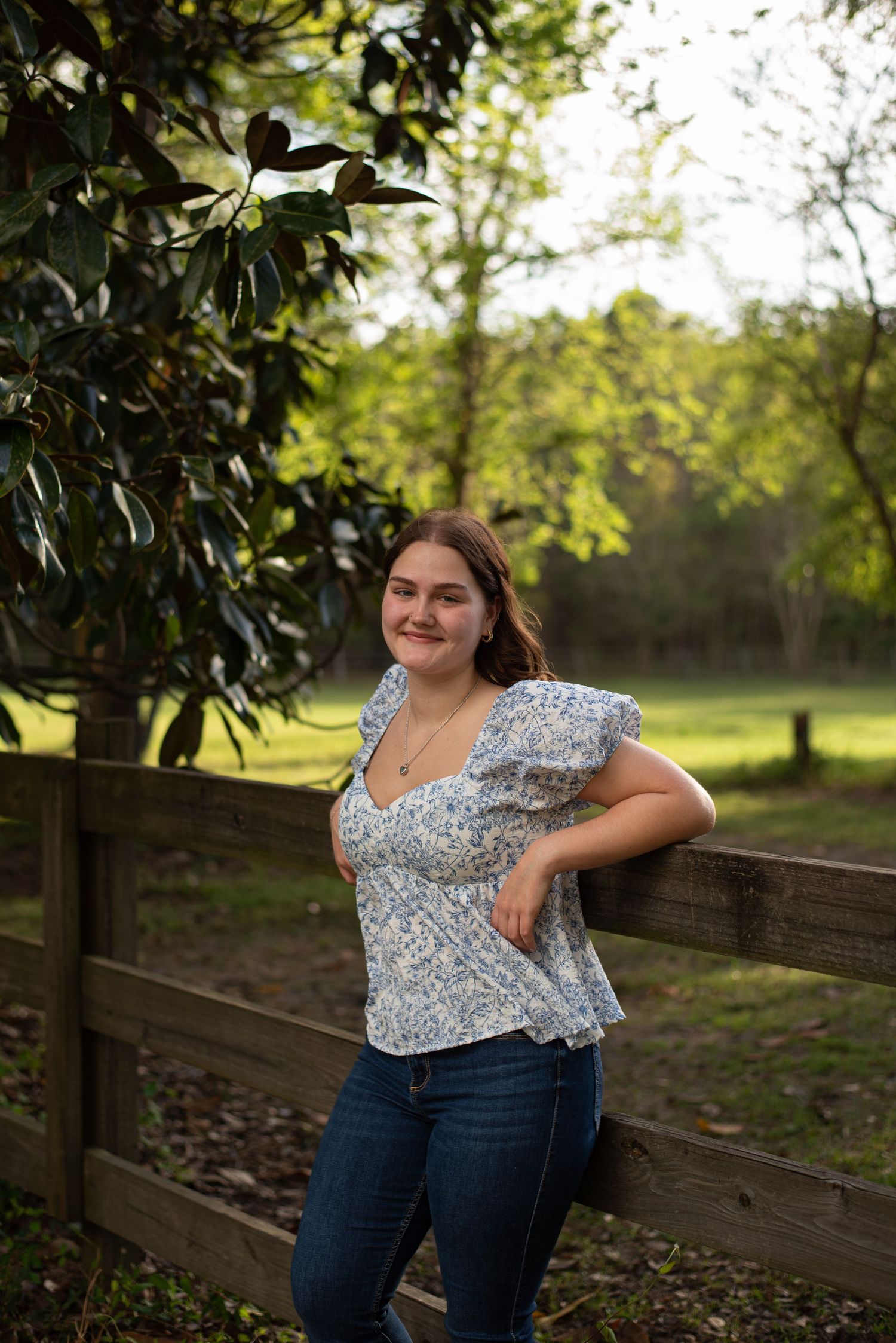 High school senior girl in front of horse pasture. Leaning on wooden fence at a farm in Ridgeland, South Carolina.