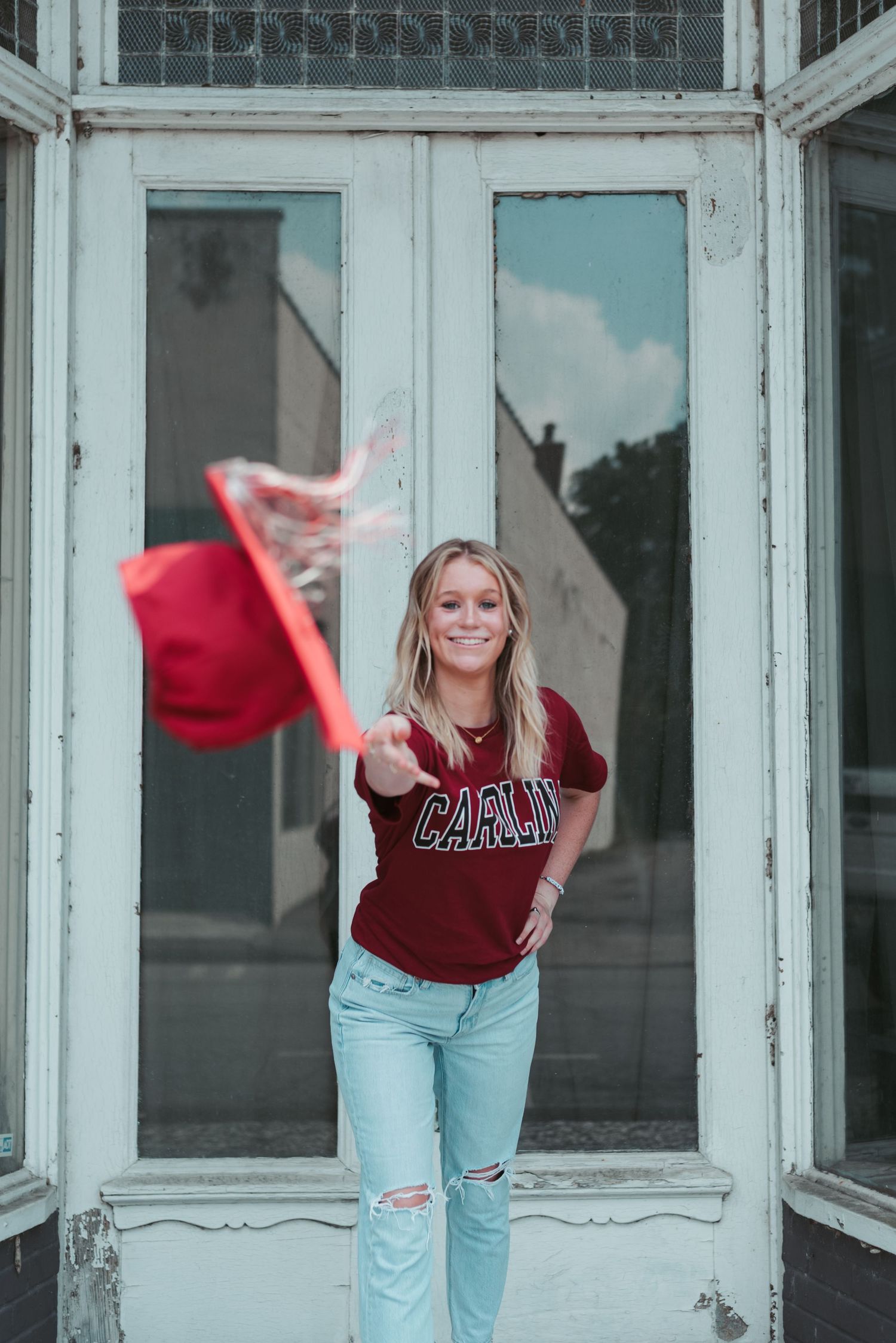 High school senior girl tossing red graduation cap at camera, wearing USC t-shirt in downtown Walterboro, South Carolina