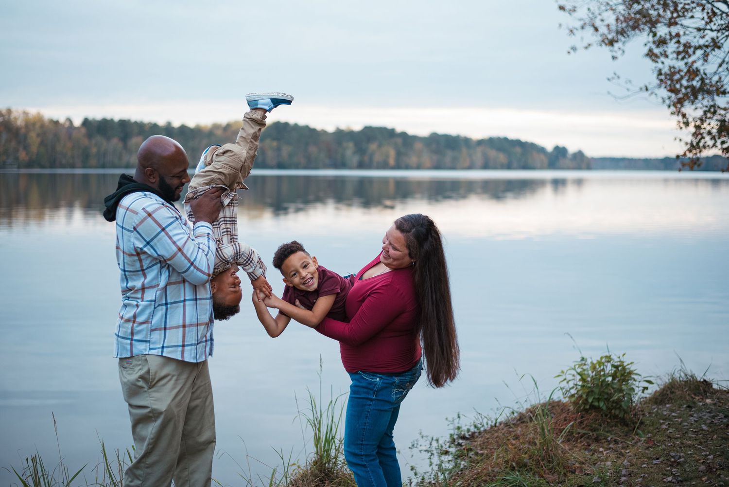 Mom and dad holding two sons in funny positions while the boys try to tickle one another. Standing in front of Lake Warren in Hampton, SC