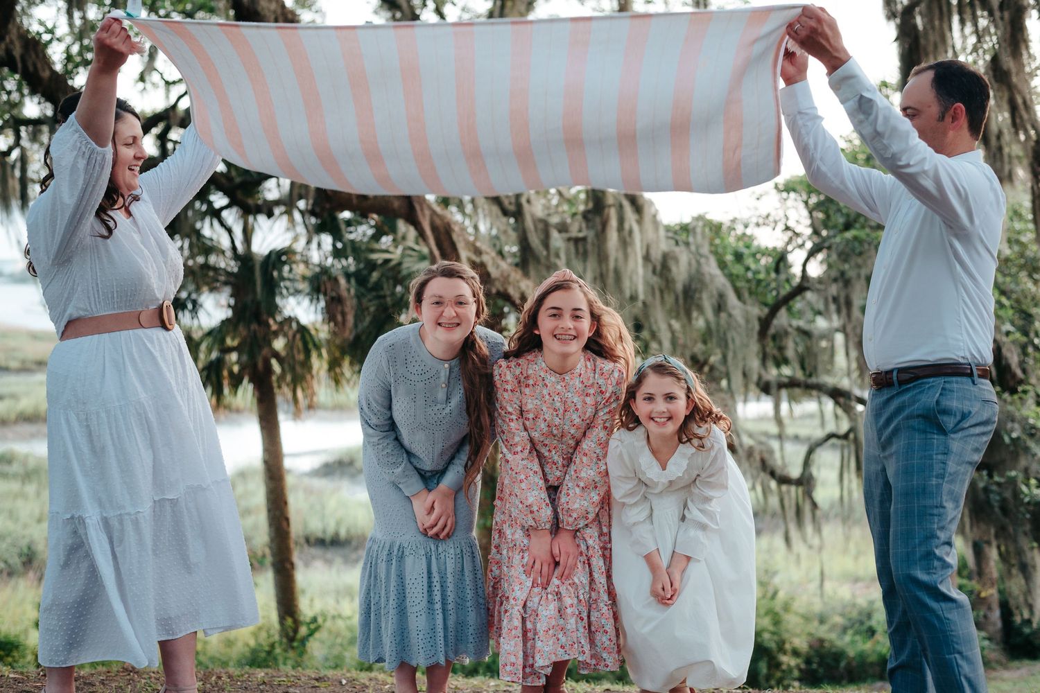 Mom and dad flapping striped blanket over three daughters in front of waterfront in Beaufort, South Carolina