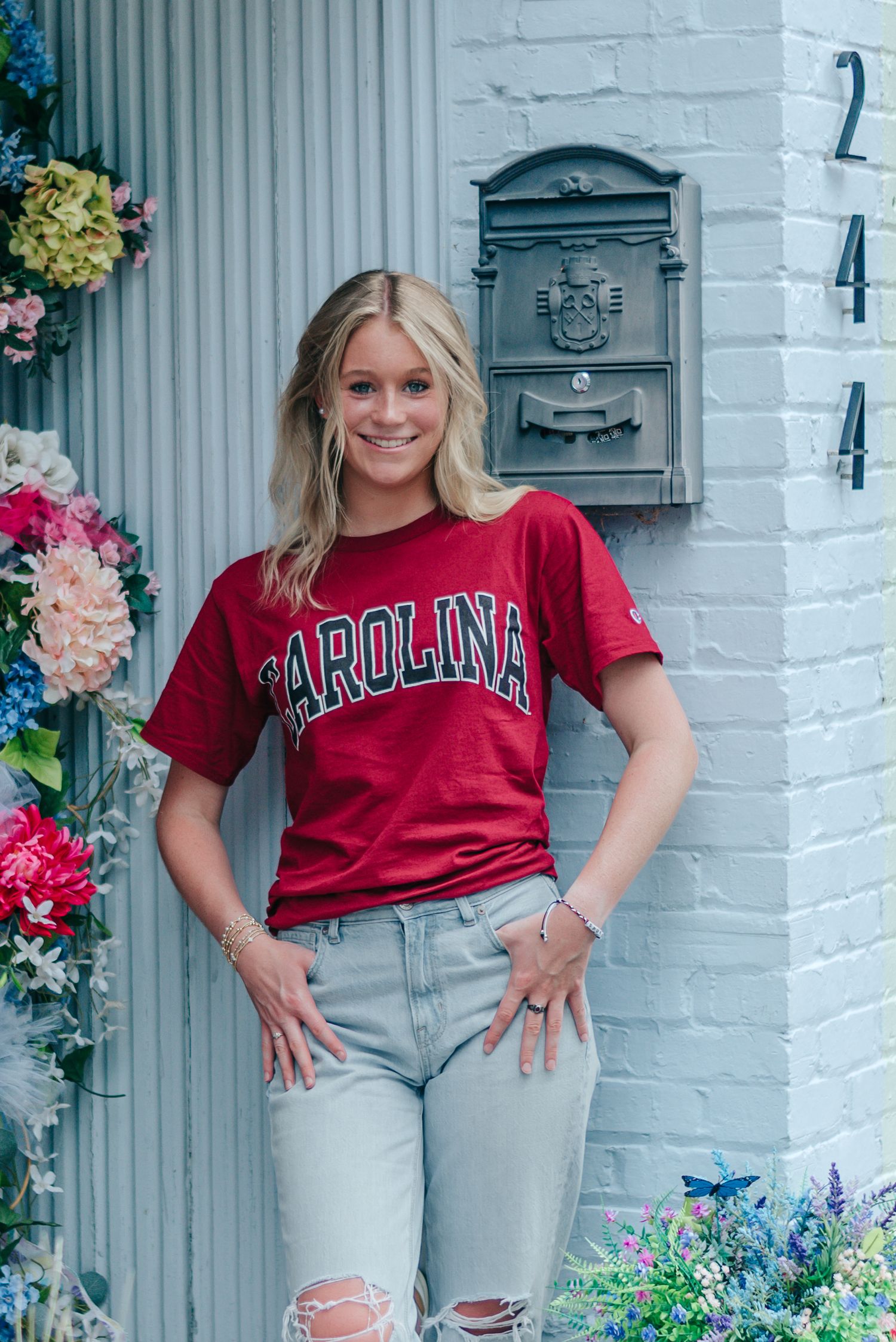 High school senior girl wearing South Carolina Gamecocks shirt, posing in front of flower garland outside boutique in Walterboro, SC.