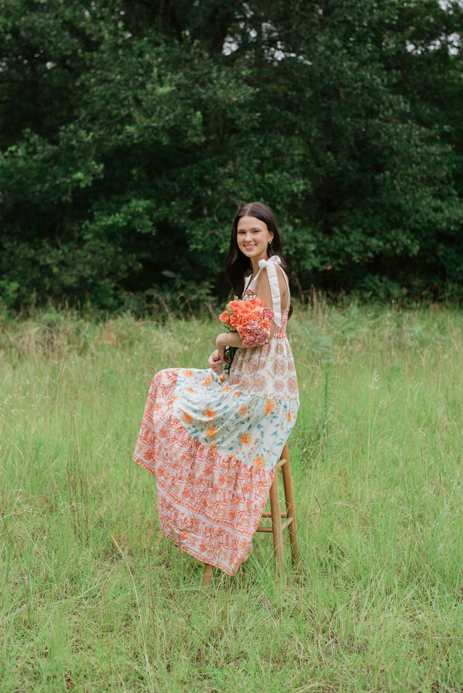 High school senior girl wearing floral dress, holding carnation and baby's breath bouquet, sitting on stool in Ridgeland, South Carolina