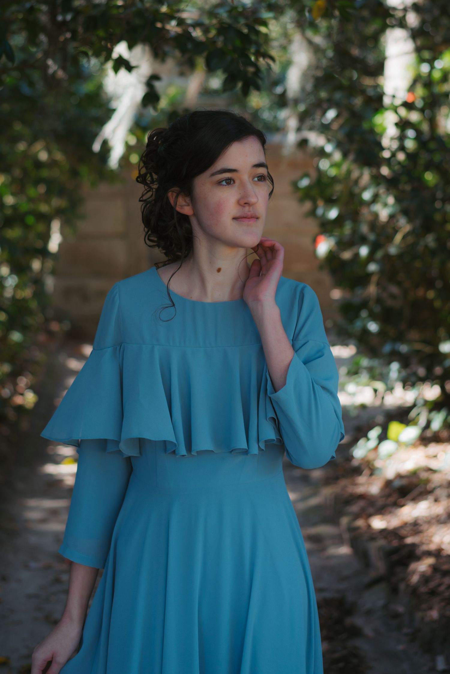 High school senior girl in flowy blue dress on shaded tree pathway at Middleton Place outside of Charleston, South Carolina