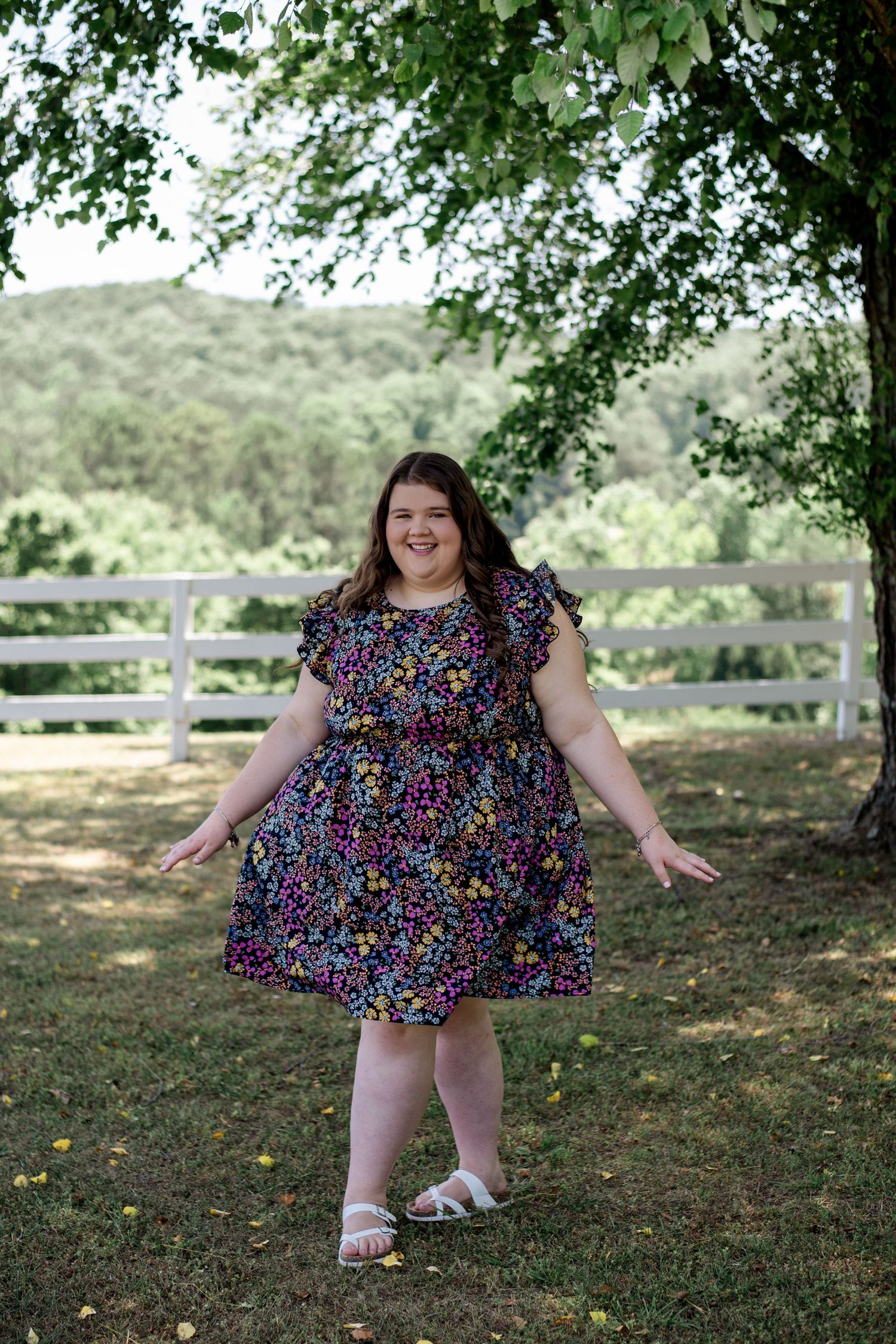 High school graduate girl in bright flower dress in front of fence on a hillside in Bartow County, Georgia.