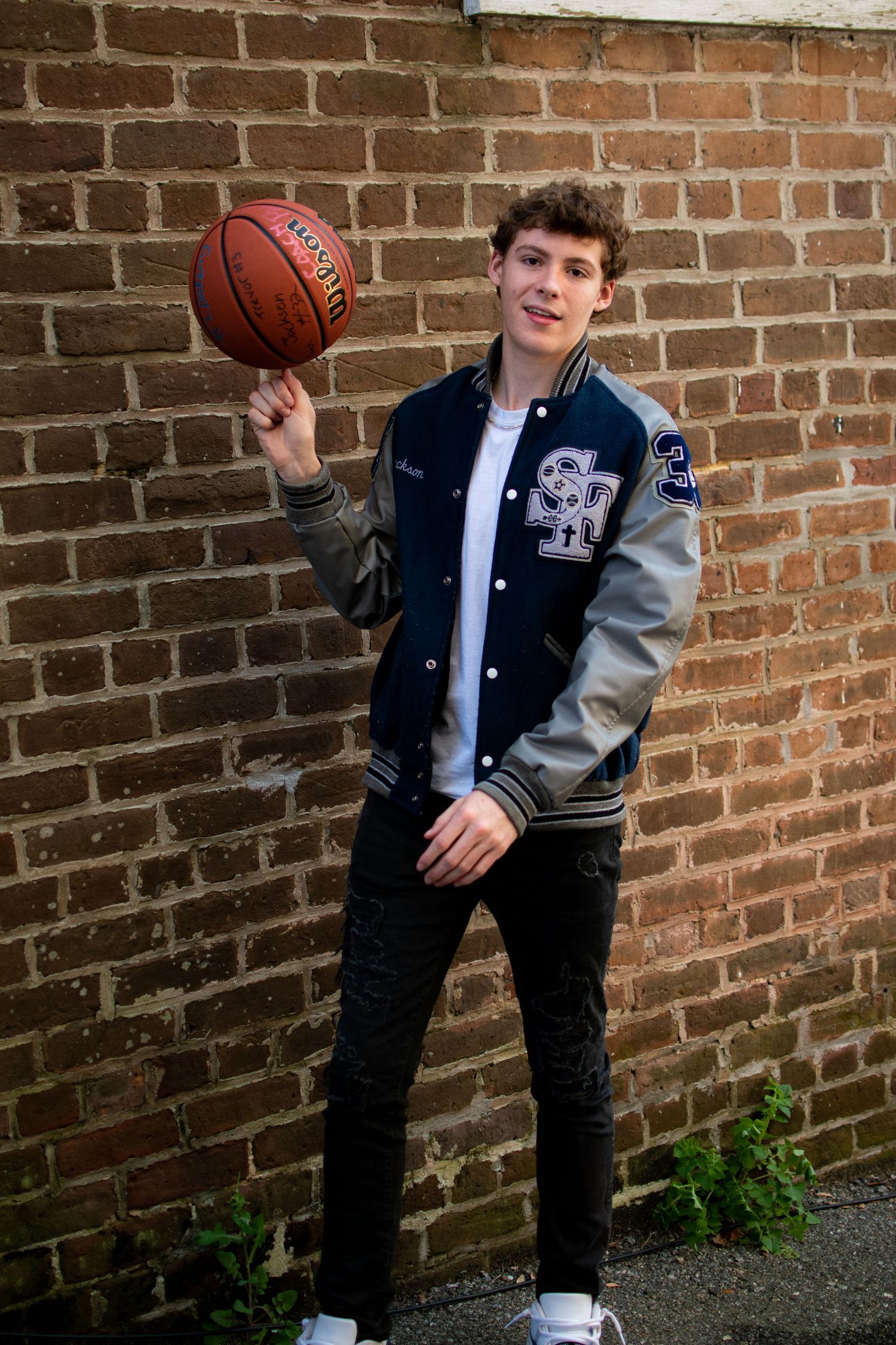 High school senior basketball player in letterman jacket, spinning ball on finger in front of brick wall in downtown Beaufort South Carolina