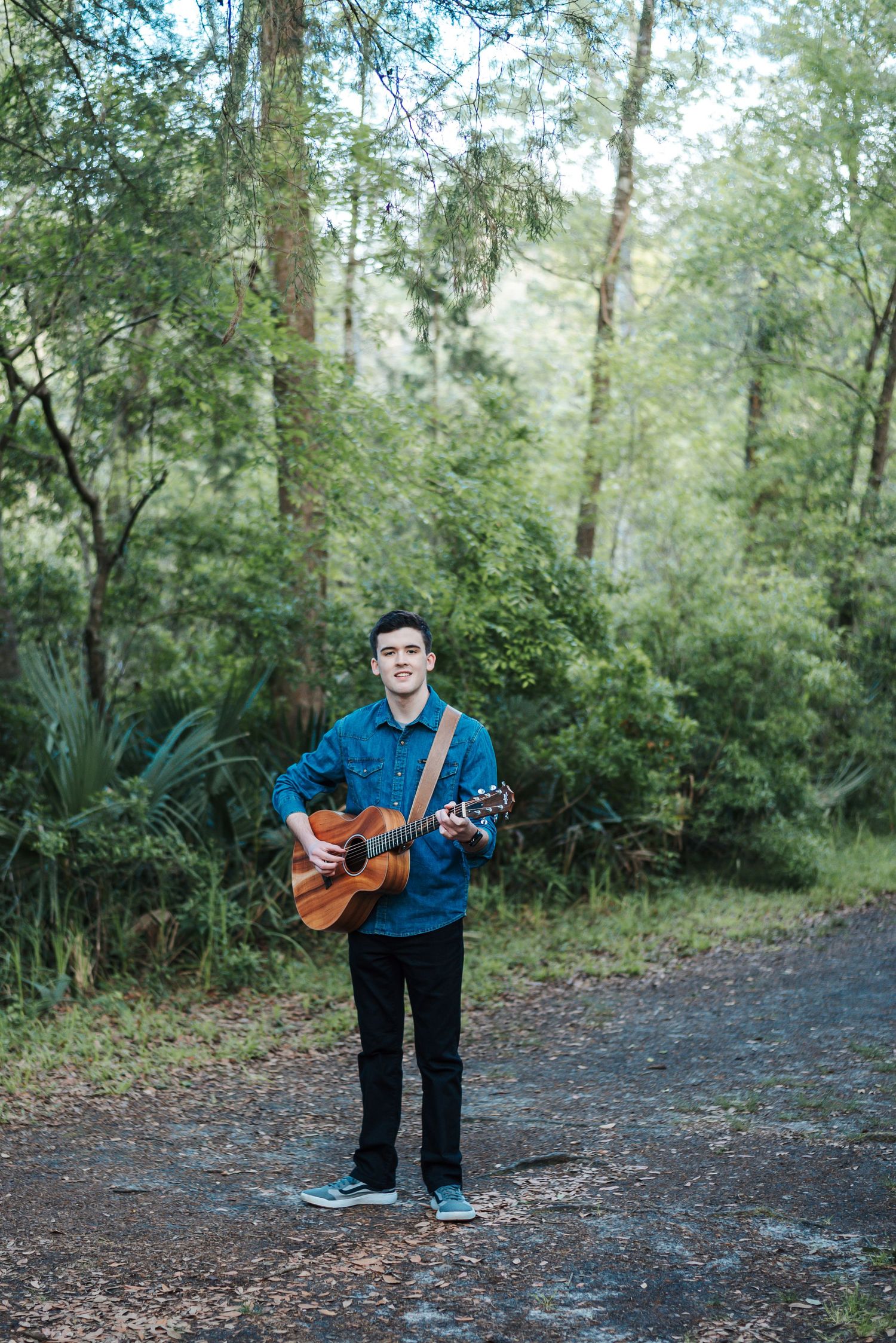High school senior guy wearing guitar in front of trees at Colonial Dorchester State Historic Site in Dorchester County, South Carolina