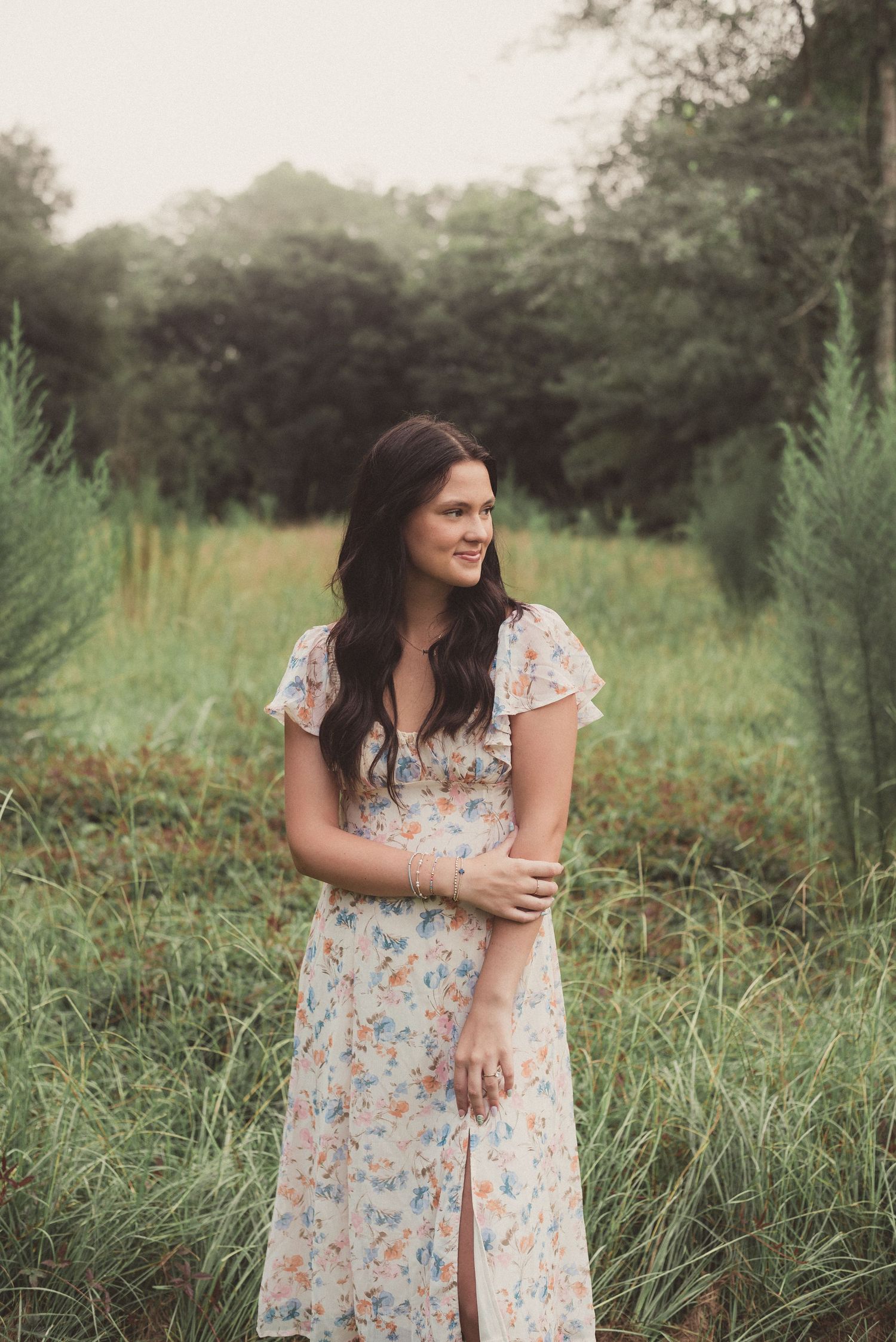 High school senior girl in floral dress, standing in front of grassy field in Ridgeland, South Carolina.