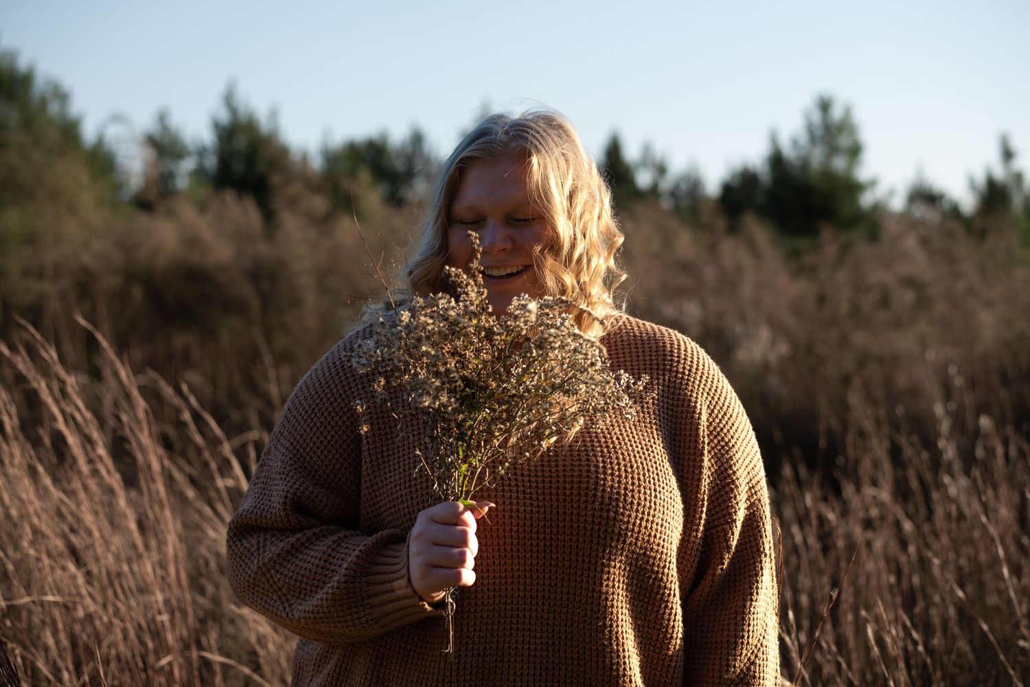 High school senior girl holding wild grass bouquet in front of tall grass and trees in Hampton County, South Carolina