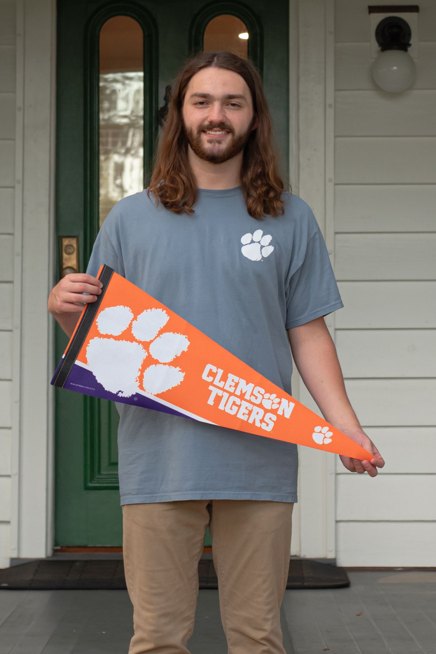 High school senior guy holding Clemson Tigers pennant in front of welcome center in Old Town Bluffton, South Carolina.