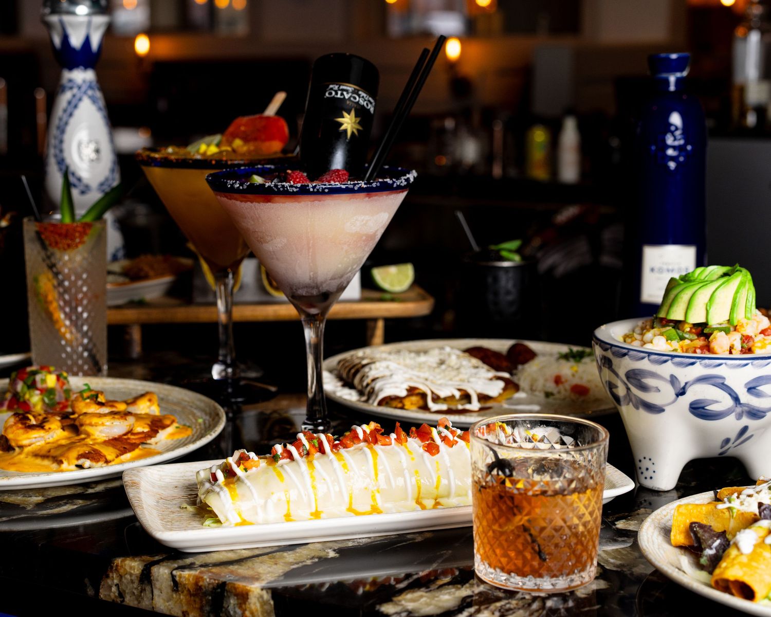 Elegantly plated food and cocktails on a restaurant table with mood lighting.