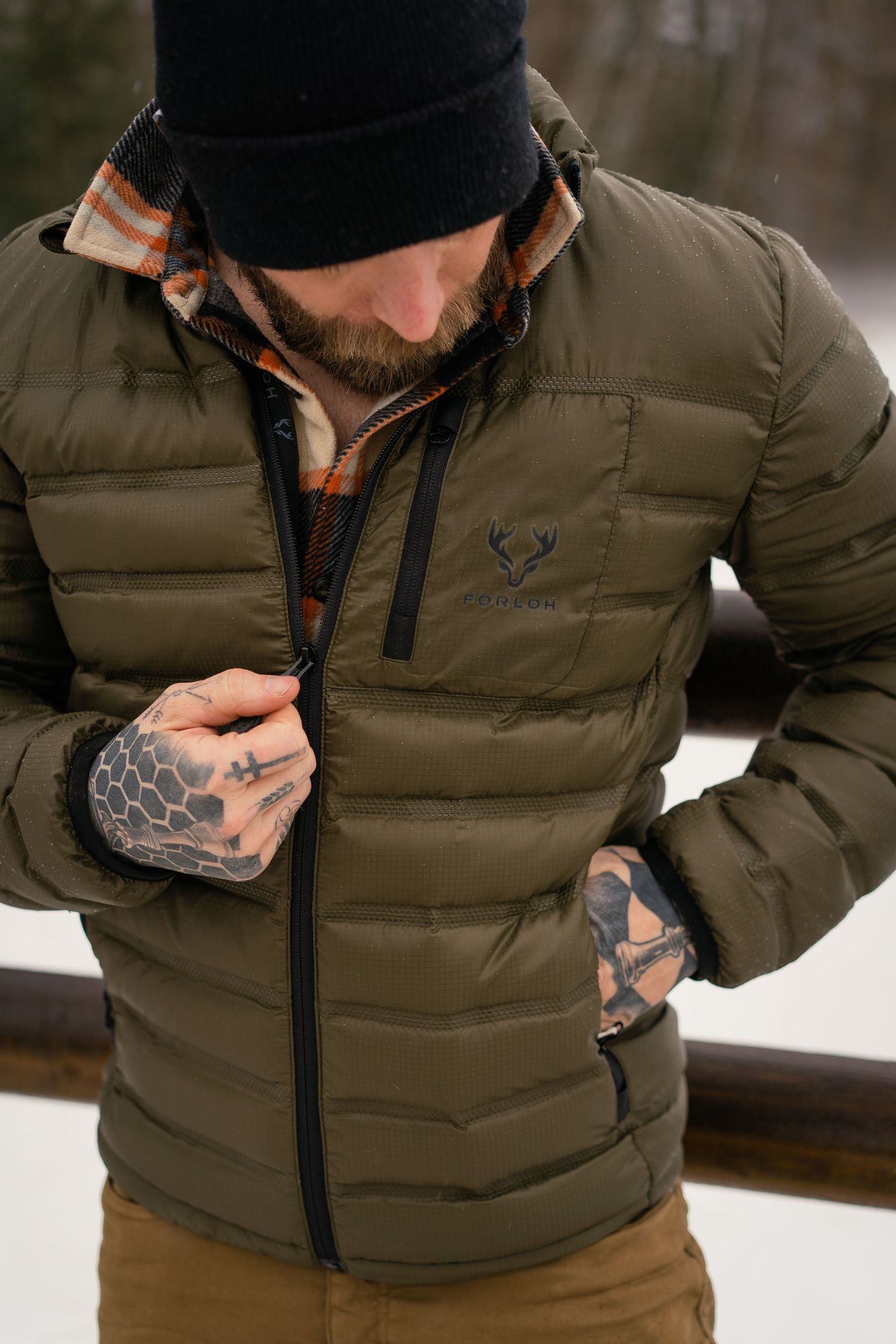 Close up of olive green puffer vest with deer logo and plaid shirt underneath.